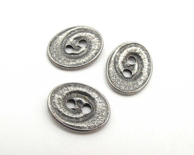 May include: Three silver oval-shaped buttons with a textured surface and two holes each.