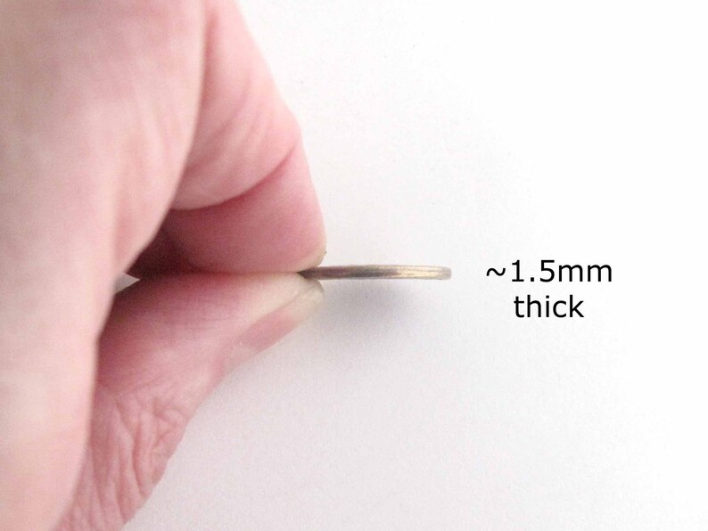 以下が含まれることがあります： 約1.5mmの厚さの薄い金属製の物体が指の間に挟まれています。その物体は硬貨または同様の円盤状のアイテムのようです。「~1.5mm thick」というテキストが物体の横に表示されています。