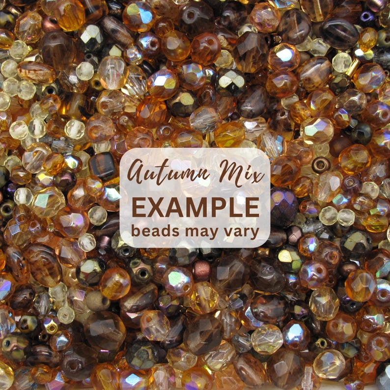 K&ouml;nnte beinhalten: Eine Sammlung verschiedener Glasperlen in Bernstein-, Braun-, Gold- und Klart&ouml;nen mit verschiedenen Formen und facettierten Texturen. Ein wei&szlig;es rechteckiges Etikett in der Mitte zeigt den Text Autumn Mix EXAMPLE beads may vary.