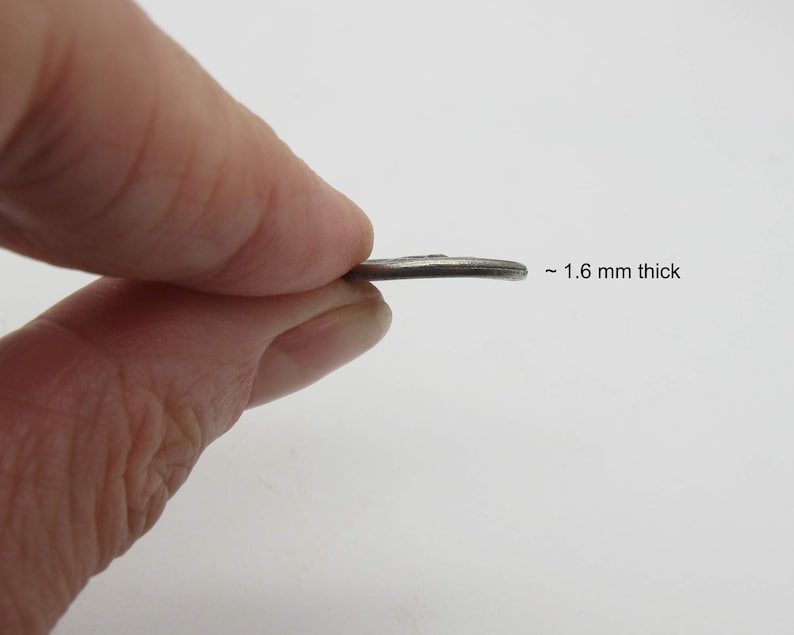 May include: A silver-colored metal disc, approximately 1.6 mm thick. The disc is being held by a finger.