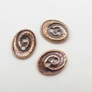 May include: Three oval-shaped copper buttons with a textured surface and two holes each.