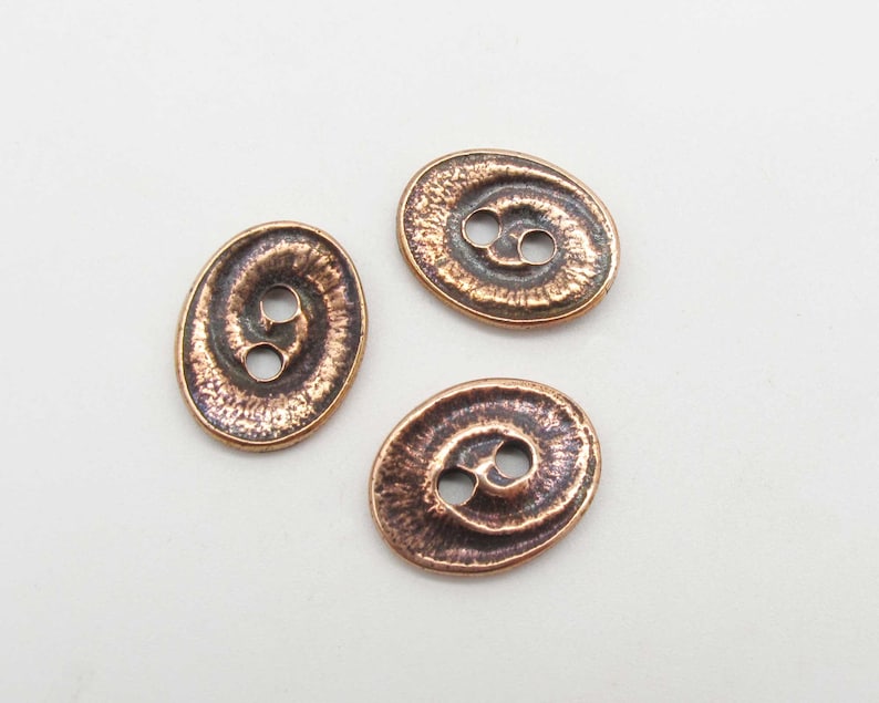 May include: Three oval-shaped copper buttons with a textured surface and two holes each.