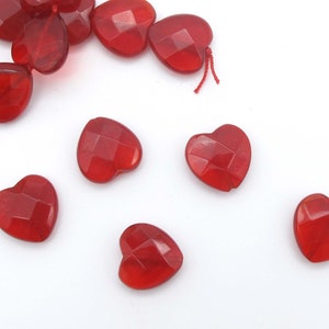 May include: Red heart-shaped beads with a faceted design. The beads are made of glass or plastic and have a translucent appearance.