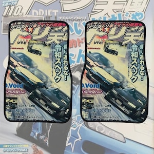 May include: A pair of car floor mats featuring a graphic print of a Japanese drift car magazine cover. The design includes images of black and yellow sports cars, Japanese text, and the word Drift Tengoku with a black border trim.