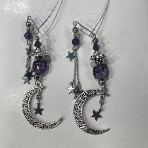 Puede incluir: Un par de pendientes de plata con cuentas de vidrio morado, estrellas plateadas y dijes de luna creciente.