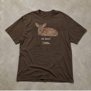 Pode incluir: Uma t-shirt de manga curta castanho-escura com um gráfico de um cervo malhado deitado. Abaixo do cervo, o texto "oh deer!" aparece em branco, seguido pelo logótipo da National Geographic em amarelo e branco centrado no peito.