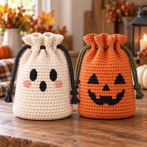May include: Two crochet drawstring bags featuring Halloween designs. One bag is cream-colored with a black ghost face and pink cheeks, featuring black drawstrings. The other is orange with a black jack-o'-lantern face and green drawstrings.