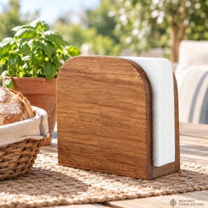May include: A wooden napkin holder with a rounded top edge, featuring a natural brown wood grain finish. The holder contains a stack of folded white paper napkins. The logo for Wooden Form Studio is visible in the bottom right corner of the image.
