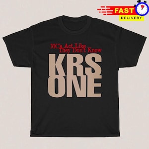 May include: A black short-sleeved t-shirt featuring the red text "MC's Act Like They Don't Know" printed above the large, beige, block-lettered text "KRS ONE" centered on the front of the garment.