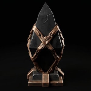 Puede incluir: Un obelisco de piedra negra puntiaguda encerrado en un marco decorativo de metal color bronce. La estructura metálica presenta bandas entrecruzadas que envuelven la piedra central, la cual tiene una grieta visible, sobre una base cuadrada.