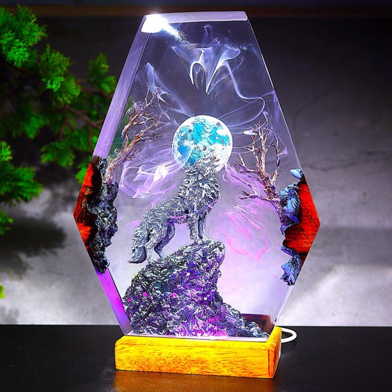 A handcrafted resin lamp with a howling wolf silhouetted against a full moon inside a coffin-shaped frame — eerie, moody desk art that doubles as a night light.