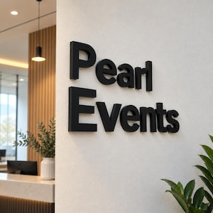 Könnte beinhalten: Ein Wandschild mit dreidimensionalen schwarzen Buchstaben, die den Schriftzug Pearl Events bilden. Die Buchstaben sind auf einer glatten, cremeweißen Wandfläche angebracht und sorgen für eine klare und professionelle Optik in einem Büro.