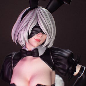 May include: A detailed figurine of a character with short white hair, wearing a black blindfold, a black bunny ear headband, and a black outfit with a white collar and a black bow tie. The figure features a mole on the cheek and red lips.