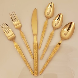 May include: Set of five gold-tone flatware with ornate floral designs. The set includes a knife, two forks, and two spoons.