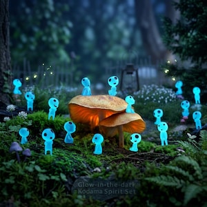 Könnte beinhalten: Eine Sammlung kleiner, leuchtend blauer Figuren mit runden Köpfen und großen schwarzen Augen, bekannt als Kodama, die um und auf orange-braunen Pilzen in einem moosigen Wald stehen. Der Text Glow-in-the-dark Kodama Spirit Set ist sichtbar.
