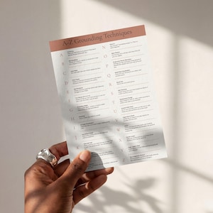 May include: A white informational card titled A-Z Grounding Techniques with a terracotta-colored header. The card lists mental health exercises from A to Z, featuring black text on a white background, providing a structured guide for mindfulness.