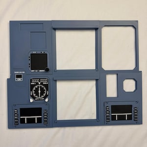 Peut inclure: Un cadre de panneau d'instruments de cockpit d'avion bleu avec plusieurs découpes rectangulaires, une jauge de navigation circulaire avec des marquages blancs et divers écrans de contrôle noirs étiquetés avec du texte dont TERR ON ND, DME-L, DME-R et BARO.