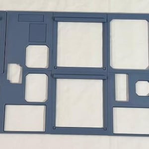 May include: A light blue aircraft cockpit instrument panel frame featuring multiple rectangular cutouts for gauges and displays, with two circular speaker grilles on the far left and right sides, constructed with a flat, matte finish.