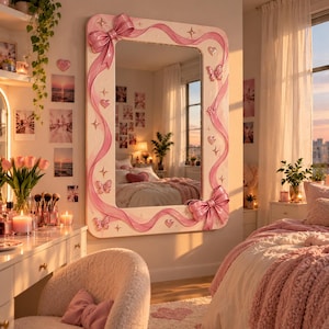 Puede incluir: Un espejo de pared rectangular con un marco blanco decorado con cintas, lazos, mariposas y corazones rosas en relieve. El marco presenta pequeños detalles de estrellas doradas. El espejo refleja el interior de un dormitorio con una cama.