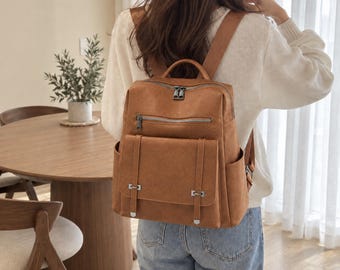 Puede incluir: Una mochila de color tostado con textura lisa, que cuenta con un asa superior, correas ajustables para los hombros, un compartimento principal con cremallera, un bolsillo frontal horizontal con cremallera y un bolsillo frontal con solapa.