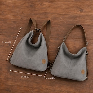 Puede incluir: Dos bolsos de lona gris con correas marrones y un peque&ntilde;o parche circular. Un bolso funciona como mochila y el otro como bolso de hombro. Las dimensiones son 34 cm de alto, 34 cm de largo y 16 cm de ancho, seg&uacute;n indican las flechas.