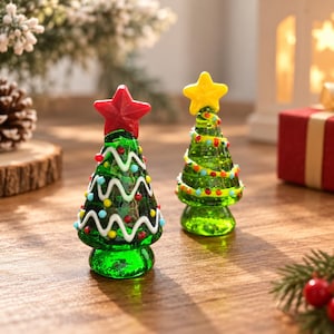 Puede incluir: Dos figuras de árbol de Navidad en miniatura de vidrio en un tono verde vibrante. Un árbol presenta una estrella roja en la punta y una guirnalda blanca ondulada, mientras que el otro tiene una estrella amarilla y una guirnalda en espiral.