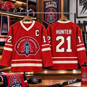 May include: A red hockey jersey featuring the New York Admirals logo on the chest, the letter C on the front, and the name HUNTER with the number 21 on the back. The jersey has white stripes on the sleeves and hem, and white numbers on the sleeves.