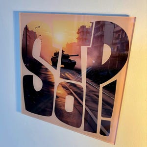 Peut inclure: Une plaque murale carrée en verre présentant le grand texte blanc "STP" et "SO!" superposé à une photographie d'un char militaire circulant dans une rue urbaine au coucher du soleil. La lumière chaude orange et jaune illumine la scène.