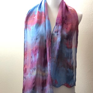 May include: A blue and pink silk scarf with a watercolor-like design. The scarf is draped over a white mannequin.