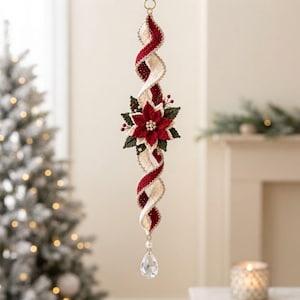 May include: A hanging spiral ornament featuring alternating cream and deep red crocheted fabric strips. A central poinsettia flower with dark green leaves, red petals, and small white beads sits in the middle, finished with a clear crystal drop.
