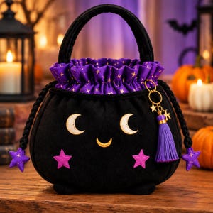 May include: A black fabric bucket bag with a rounded shape, featuring a purple ruffled top with gold star patterns. The front displays two embroidered crescent moons and a small smile, with two pink stars below. It has a purple tassel and star charm.