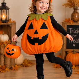 May include: A bright orange pumpkin costume featuring a black jack-o'-lantern face, a green leaf collar, and a matching pumpkin hat. The outfit is worn over a black long-sleeve shirt and black leggings, paired with black boots and a plastic pumpkin bucket.