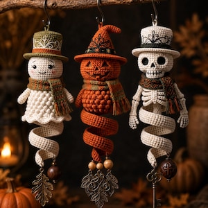 Puede incluir: Tres adornos colgantes de ganchillo que representan un fantasma con sombrero de copa verde, una calabaza con sombrero de bruja naranja y un esqueleto con sombrero de copa blanco. Cada figura lleva una bufanda y una base en espiral con dijes.
