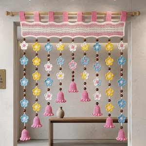 May include: A hand-crocheted toran hanging from a wooden rod, featuring a pink and white scalloped top border. Multiple vertical strands consist of brown wooden beads interspersed with small crocheted flowers in pink, yellow, white, and blue.