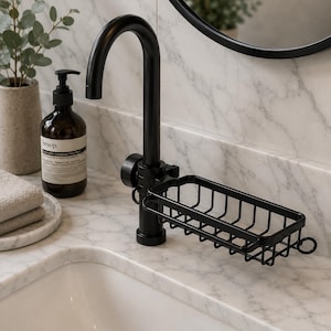 Puede incluir: Un accesorio de grifo de metal negro mate con una cesta de alambre rectangular integrada para jabón. El accesorio tiene un diseño de cuello curvo e incluye un pequeño detalle de anillo circular en el lateral del marco de la cesta para colgar.