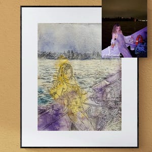 Op de afbeelding: Een ingelijste kunstdruk met een lijntekening van een persoon in een boot op het water, met een kleine inzetfoto in de rechterbovenhoek. De print staat op een roze modulaire kast die gevuld is met diverse boeken en stapels media.