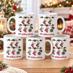 May include: Five white ceramic mugs featuring a festive Christmas design with hanging stockings labeled Liam, Anna, Lily, and David, plus a paw print stocking. The text The William Family is printed in red script at the bottom of each mug.