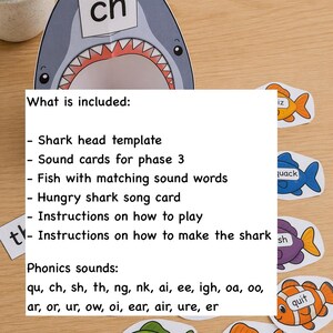 May include: A paper shark head template with the letters ch, accompanied by colorful fish cutouts labeled with phonics words like path, chop, and quit. The text lists included items such as a shark head template, sound cards, fish, a song card, and instructions for phonics sounds including qu, ch, sh, th, ng, nk, ai, ee, igh, oa, oo, ar, or, ur, ow, oi, ear, air, ure, and er.
