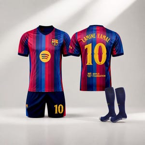 Puede incluir: Un conjunto de fútbol del FC Barcelona que incluye una camiseta a rayas azules y rojas con el logo de Spotify y el escudo del equipo, pantalones cortos azules a juego con el número 10 y calcetines azules. La espalda muestra Lamine Yamal y el 10.