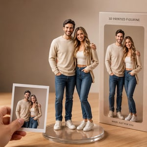 May include: A 3D printed figurine of a couple standing together on a clear circular base. The figurine is displayed next to its packaging box labeled 3D PRINTED FIGURINE and MADE JUST FOR YOU, with a small photo of the couple held in the foreground.