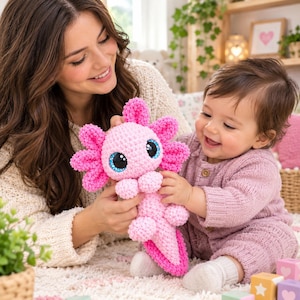 Pode incluir: Um peluche de axolote feito à mão em croché com um corpo rosa claro, guelras com franjas rosa brilhante e grandes olhos pretos brilhantes com detalhes azuis. A criatura tem uma superfície de fio macio e texturizado e uma cauda longa e plana.