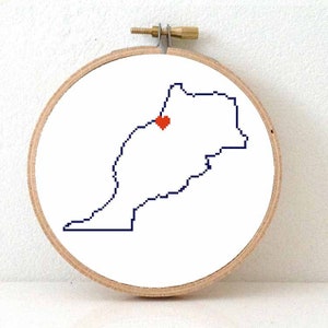 Può includere: Un telaio da ricamo rotondo con un tessuto bianco con un contorno pixelato di un paese in blu scuro, con un indicatore rosso a forma di cuore. Il telaio è in legno e ha una vite in ottone e hardware in metallo.