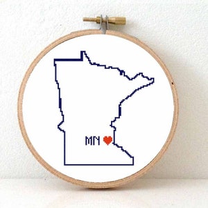 May include: A white embroidery hoop with a blue outline of the state of Minnesota and a red heart in the approximate location of Minneapolis. The text "MN" is written below the heart.