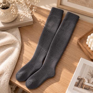 Può includere: Un paio di calze sopra il ginocchio color grigio antracite scuro, realizzate in un tessuto a maglia morbido e testurizzato, con un bordo a coste sulla parte superiore. Le calze sono lunghe, dalla punta fino all'apertura a coste superiore.