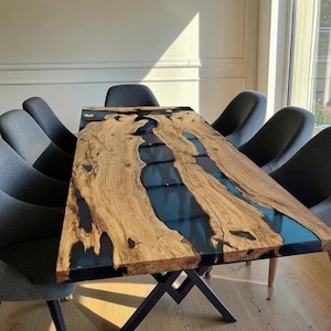 May include: A rectangular dining table featuring a live edge wood slab with a central dark blue resin river inlay. The table is supported by a black metal X-shaped base and is surrounded by eight dark grey upholstered chairs with curved backs.