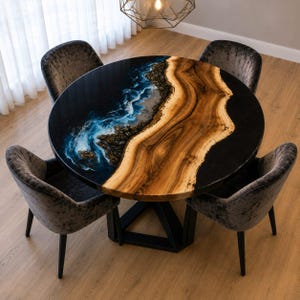 May include: A round dining table featuring a natural wood slab with a live edge, integrated with a blue and white resin design resembling ocean waves and a black resin border, supported by a black metal base with four grey velvet chairs.