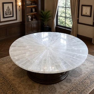 Puede incluir: Una gran mesa de comedor circular con un tablero de piedra de selenita blanca pulida que presenta un patrón radial similar a un sol con segmentos cristalinos. La mesa se apoya sobre una base de pedestal cilíndrica de madera marrón.