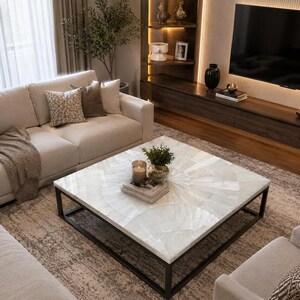 Puede incluir: Una mesa de centro cuadrada con un tablero de piedra blanca con patrón de abanico y un marco de metal negro. La mesa está situada en una sala de estar y sostiene una pequeña planta en maceta, un portavelas de cristal y libros.