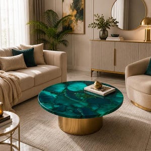 Op de afbeelding: Een ronde salontafel met een levendig groen agaatstenen blad met natuurlijke kristallijne patronen en diepe blauwgroene aders. De tafel wordt ondersteund door een massieve, cilindrische basis van goudkleurig metaal voor een stabiele ondergrond.