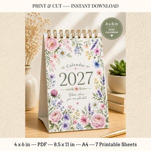 Könnte beinhalten: Ein 2027 Tischkalender mit goldener Spiralbindung, verziert mit einem Blumenrand aus rosa, violetten und gelben Wildblumen. Der Text lautet Calendar 2027 und Bloom where you are planted. Der Kalender misst 10,16 mal 15,24 cm.